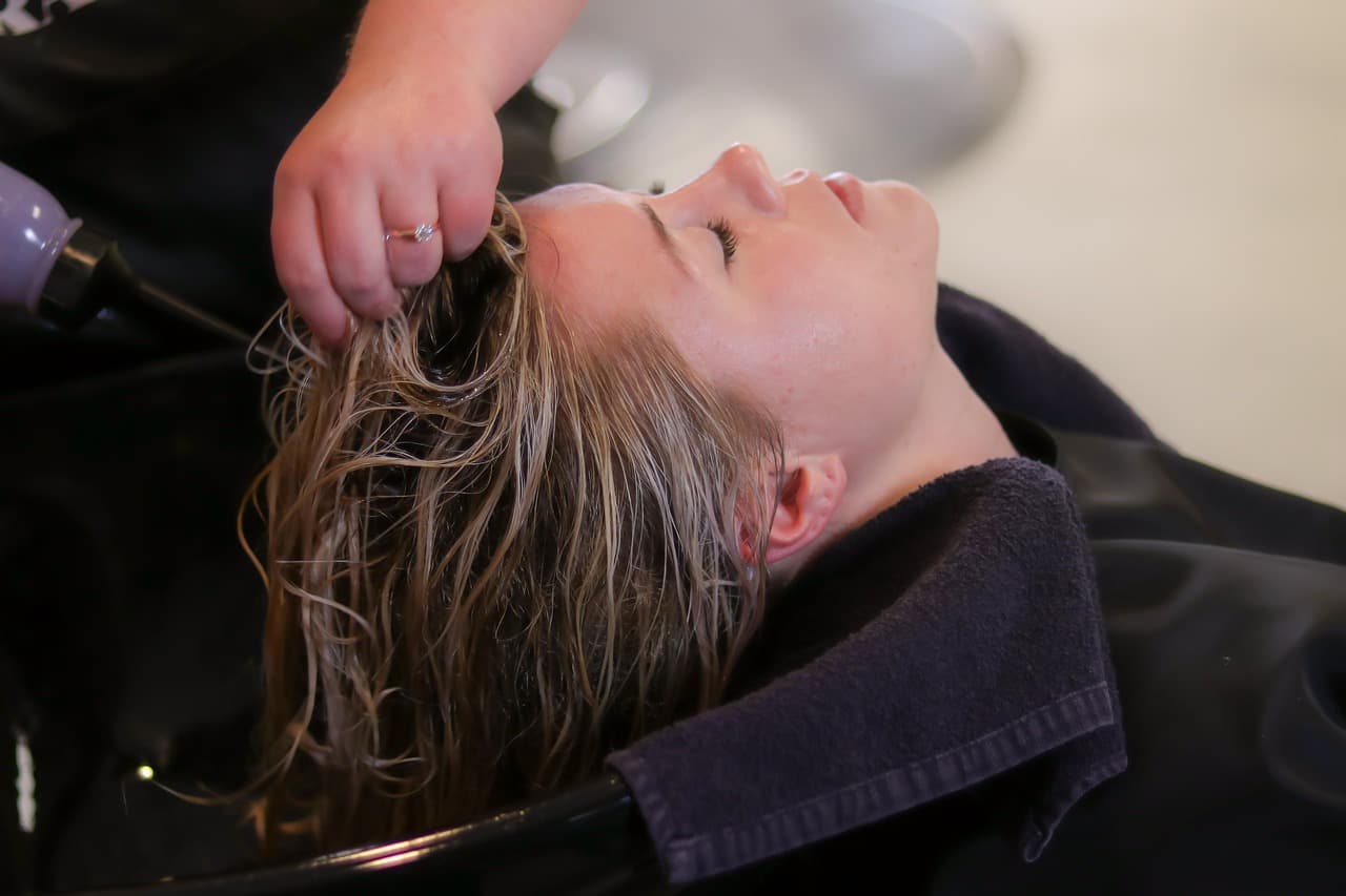 A client lying back at a basin while her hair is washed and her scalp massaged