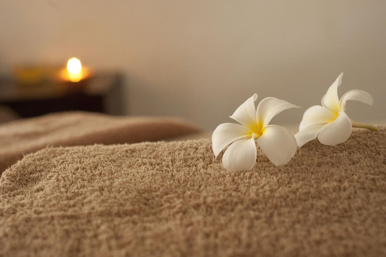 A rolled towel with frangipani flowers and a candle in a treatment room